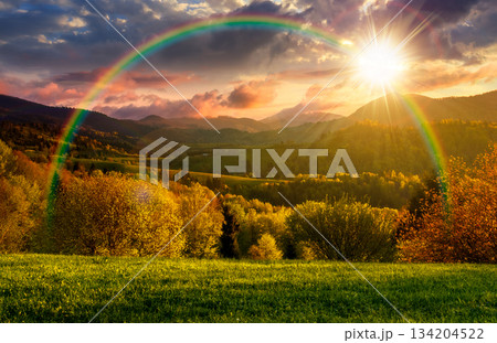 forested hills in spring at sunset. beautiful scenery in mountains in evening light. rolling countryside landscape. remote rural region in highlands. timeless nostalgia book cover with rainbow 134204522