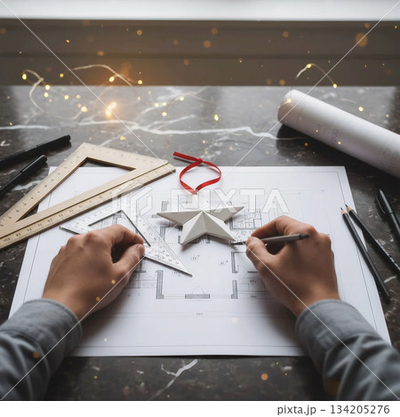 architect's hands drawing a house plan decorated with a white origami star and a christmas ribbon architect's hands drawing a house plan decorated with a white origami star and a christmas ribbon 134205276