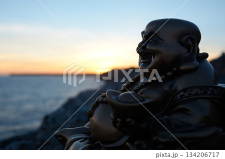 Buddha figure on some rocks, in the sunset, on the sea 134206717