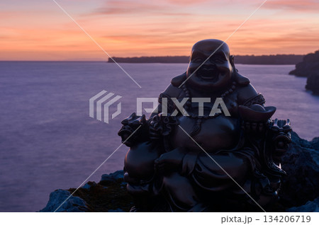 Buddha figure on some rocks, in the sunset, on the sea 134206719