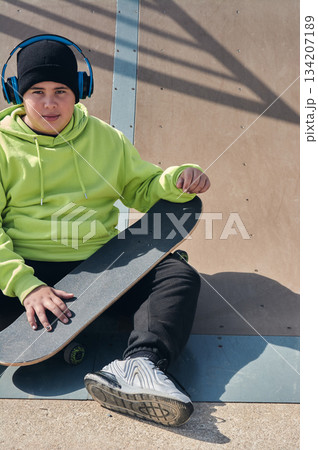 young, teenager, with skateboard sitting on the track, with headphones young, teenager, with skateboard sitting on the track, with headphones 134207189