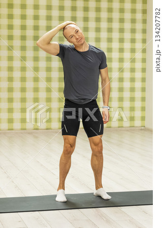 Caucasian man stretching neck muscles performing warmup exercise in indoor fitness studio releasing tension after work and improving mobility. Healthy lifestyle and daily routine. Caucasian man stretching neck muscles performing warmup exercise in indoor fitness studio releasing tension after work and improving mobility. Healthy lifestyle and daily routine. 134207782