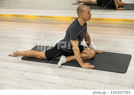 Adult caucasian male performing yoga pigeon pose on mat, stretching hips and improving flexibility in studio. Adult caucasian male performing yoga pigeon pose on mat, stretching hips and improving flexibility in studio. 134207785
