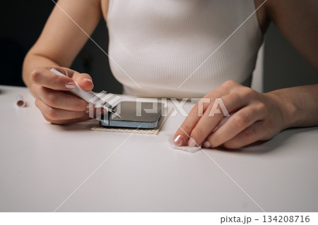 Woman cleaning microphone of smartphone with specialized brush tool, focusing on maintaining optimal audio quality and ensuring hygiene for better communication. Concept of mobile phone service. 134208716