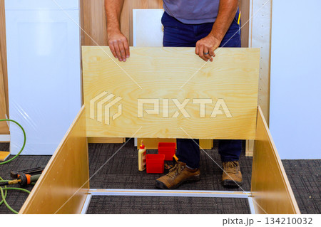 Worker builds wooden cabinet at construction site with tools materials around him 134210032