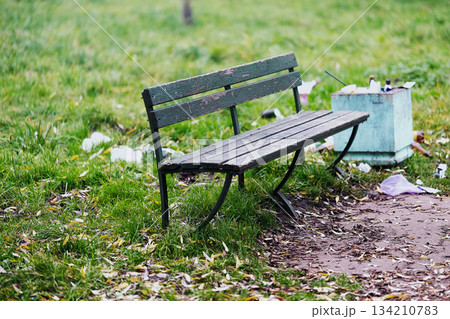 A trash can is positioned right next to a bench that is located in a park. High quality photo 134210783