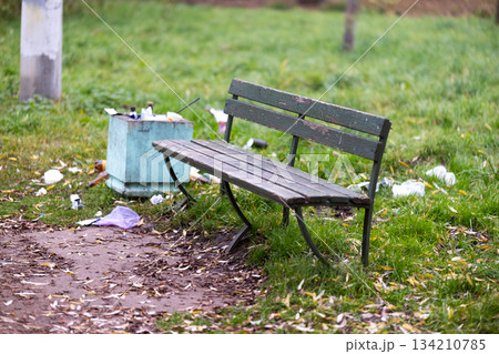 A trash can is positioned right next to a bench that is located in a park. High quality photo A trash can is positioned right next to a bench that is located in a park. High quality photo 134210785