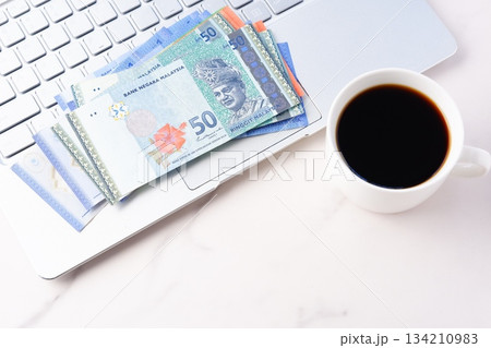マレーシアの通貨リンギット（MYR）の紙幣とノートパソコン、淹れたてのコーヒーが入ったコーヒーカップ 134210983