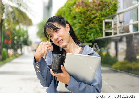 Young woman, person on street, busy lifestyle, travel business work, outdoor professional communicating on phone, holding laptop and coffee, managing urban tasks, navigating city environment. 134212025