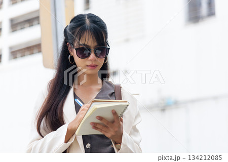 Business woman, person on city street enjoying outdoor work lifestyle, stylish young professional diligently takes notes, planning future travel goals. 134212085