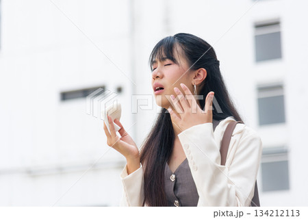 Business woman working outdoors, urban street lifestyle, feeling unwell, suffering allergy symptoms, using tissue, showing facial discomfort, dealing with seasonal cold symptoms. 134212113