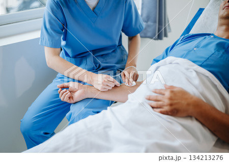 Friendly Female Head Nurse Making Rounds does Checkup on Patient Resting in Bed. She Checks tablet while Man Fully Recovering after Successful Surgery in hospital 134213276
