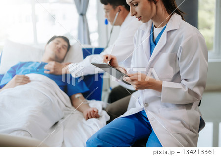 Two doctors talking to a patient lying in his bed with receiving saline solution Two doctors talking to a patient lying in his bed with receiving saline solution 134213361