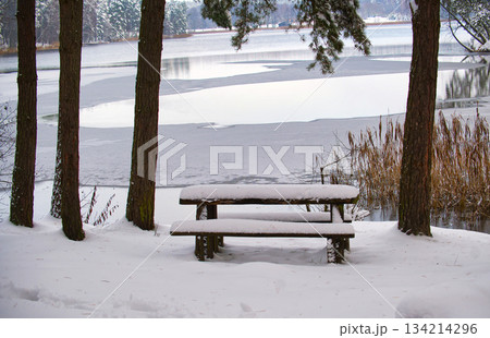 Snow-covered picnic table overlooking a frozen lake in winter Snow-covered picnic table overlooking a frozen lake in winter 134214296