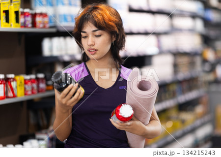 Young girl choosing a bottle of vitamins in sports nutrition store 134215243