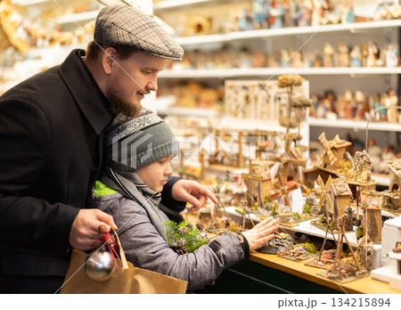 Dad and son standing near counter at Christmas market fair, choosing figurines for nativity scene 134215894