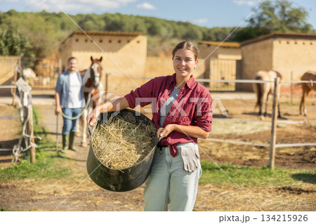 Young woman with bucket of hay feed for horse Young woman with bucket of hay feed for horse 134215926