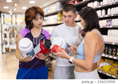 Two women and man choosing jar of sports nutrition Two women and man choosing jar of sports nutrition 134215958