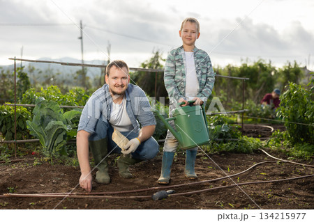 Young man with boy planting seeds in field 134215977