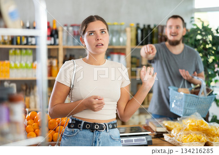 Sullen girl stands with arms crossed on chest, swears with husband and listens to mans accusations 134216285