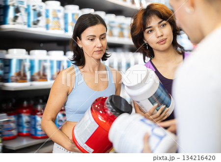 Young guy and women choosing protein powder jar in sports nutrition store Young guy and women choosing protein powder jar in sports nutrition store 134216420