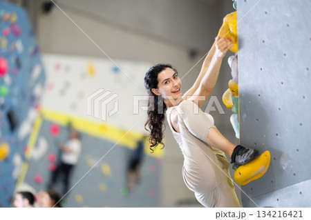 Motivated young girl climbing without ropes and harnesses on artificial bouldering wall in fitness center 134216421