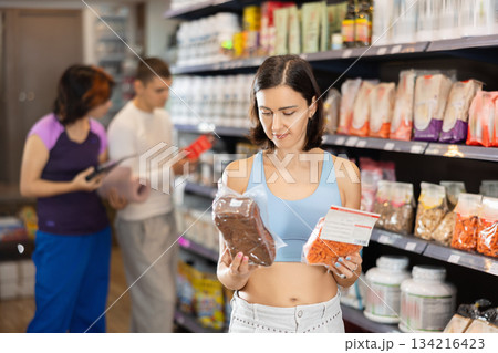 Middle-aged woman choosing whole-grain pasta or bread in sports nutrition store Middle-aged woman choosing whole-grain pasta or bread in sports nutrition store 134216423