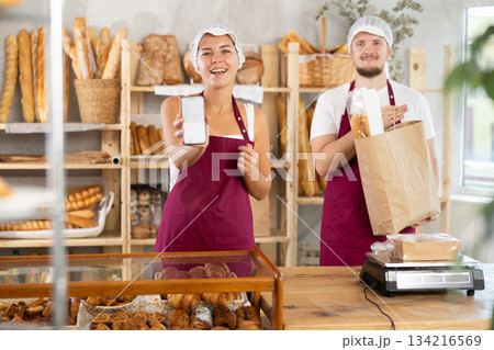 Saleswoman displays phone app standing next to salesman with baguettes 134216569
