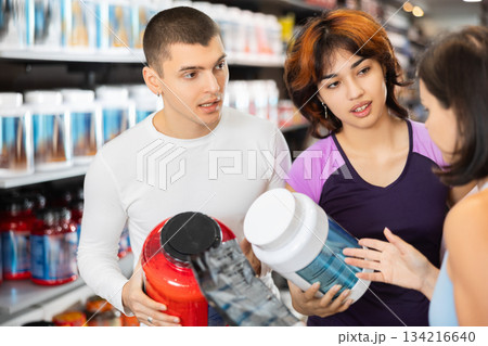 Young guy and women choosing protein powder jar in sports nutrition store Young guy and women choosing protein powder jar in sports nutrition store 134216640