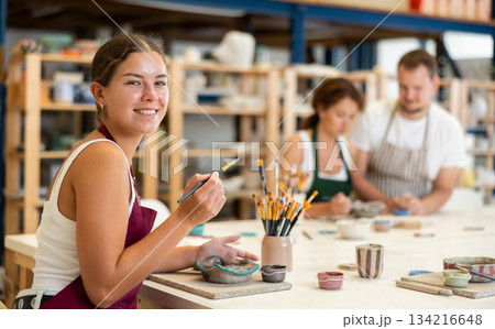 During workshop at master class, female employee paints clay vessel plate 134216648