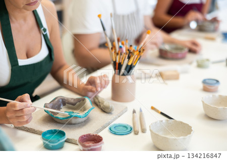 Close up girl paints bowl of clay during master class, top view. Close up girl paints bowl of clay during master class, top view. 134216847