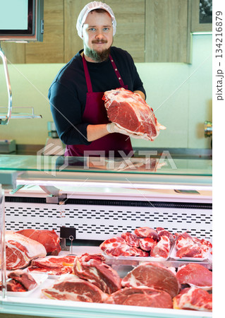 Male butcher putting raw meat on supermarket display 134216879