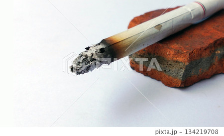Close-Up of a Burning Cigarette with Ash on a Brick Surface 134219708