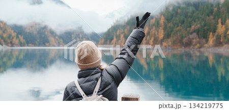 Happy woman traveler travel in jiuzhaigou national park in Sichuan, China. Tourist sightseeing Long lake and snow mountain in Autumn season. Famous Landmark and Vacation near Chengdu, China 134219775