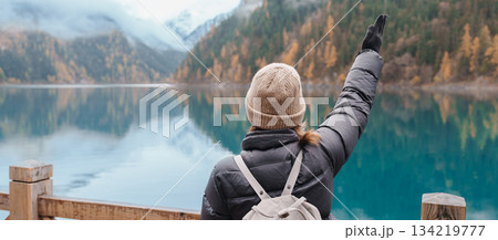 Happy woman traveler travel in jiuzhaigou national park in Sichuan, China. Tourist sightseeing Long lake and snow mountain in Autumn season. Famous Landmark and Vacation near Chengdu, China Happy woman traveler travel in jiuzhaigou national park in Sichuan, China. Tourist sightseeing Long lake and snow mountain in Autumn season. Famous Landmark and Vacation near Chengdu, China 134219777