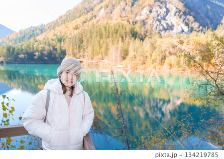 Happy woman traveler travel in jiuzhaigou national park in Sichuan, China. Tourist sightseeing Arrow Bamboo lake and snow mountain in Autumn season. Famous Landmark and Vacation near Chengdu, China 134219785