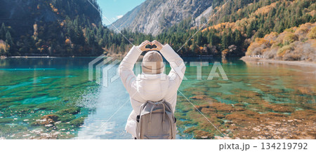 Happy woman traveler travel in jiuzhaigou national park in Sichuan, China. Tourist sightseeing Five Flower lake and snow mountain in Autumn season. Famous Landmark and Vacation near Chengdu, China 134219792