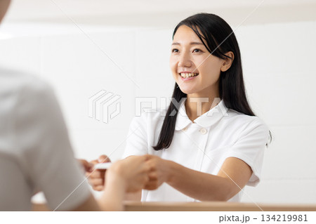 受付でカードを受け取る白衣姿の女性 受付でカードを受け取る白衣姿の女性 134219981