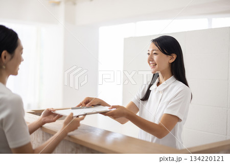 受付で問診票を手渡す白衣姿の女性 受付で問診票を手渡す白衣姿の女性 134220121