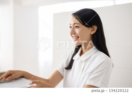 受付で問診票を手渡す白衣姿の女性 134220122