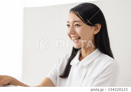 受付で問診票を手渡す白衣姿の女性 134220123