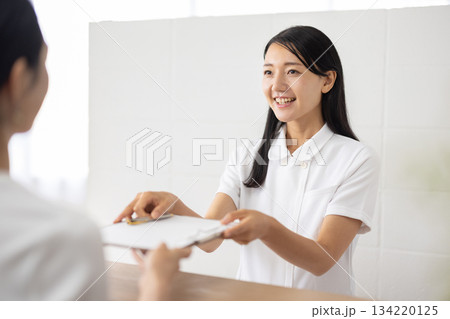 受付で問診票を手渡す白衣姿の女性 受付で問診票を手渡す白衣姿の女性 134220125