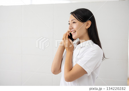 スマートフォンを耳に当てる白衣姿の女性 スマートフォンを耳に当てる白衣姿の女性 134220282