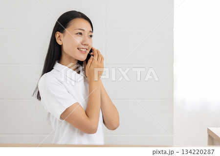 スマートフォンを耳に当てる白衣姿の女性 134220287