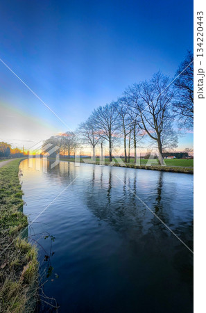 The Serene Sunset Reflection on the Calm River offers a picturesque view of natures beauty The Serene Sunset Reflection on the Calm River offers a picturesque view of natures beauty 134220443