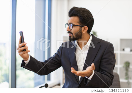 An Arab businessman in a suit looks frustrated while on a video call using his smartphone An Arab businessman in a suit looks frustrated while on a video call using his smartphone 134221159