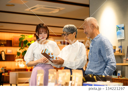 店員と夫婦がお土産を選ぶ 134221297
