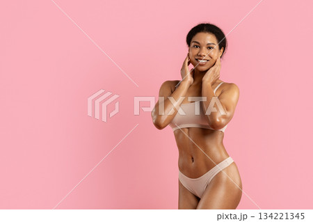 Young black woman posing playfully in beige underwear on pink studio background 134221345