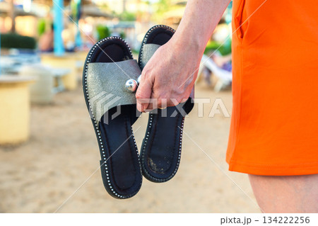 Women's summer sandals in the hands of a woman on the beach 134222256
