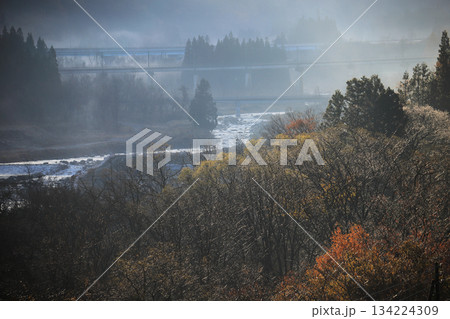 山間を流れる河川と靄のかかった幻想的な森林 遠くに鉄道の架線が見える 134224309